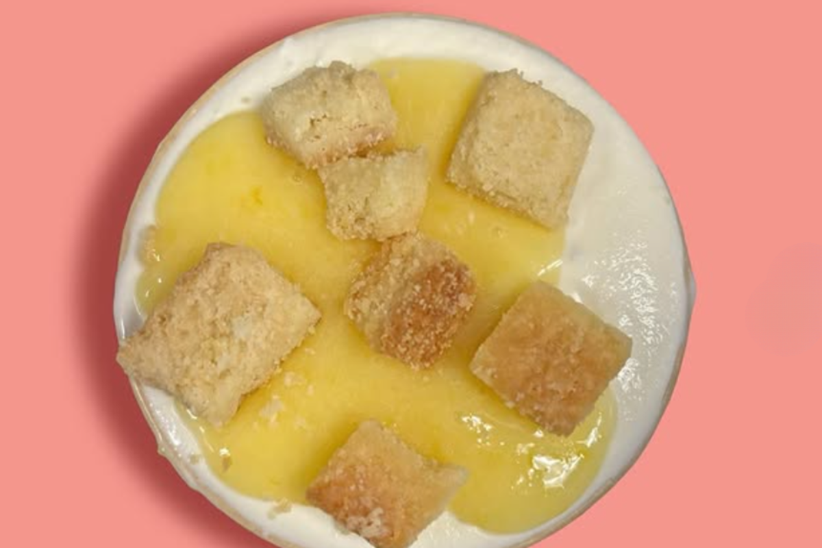 Creamy Labneh Lemon ice cream topped with lemon curd and chunks of shortbread, served in a cup against a pink background.