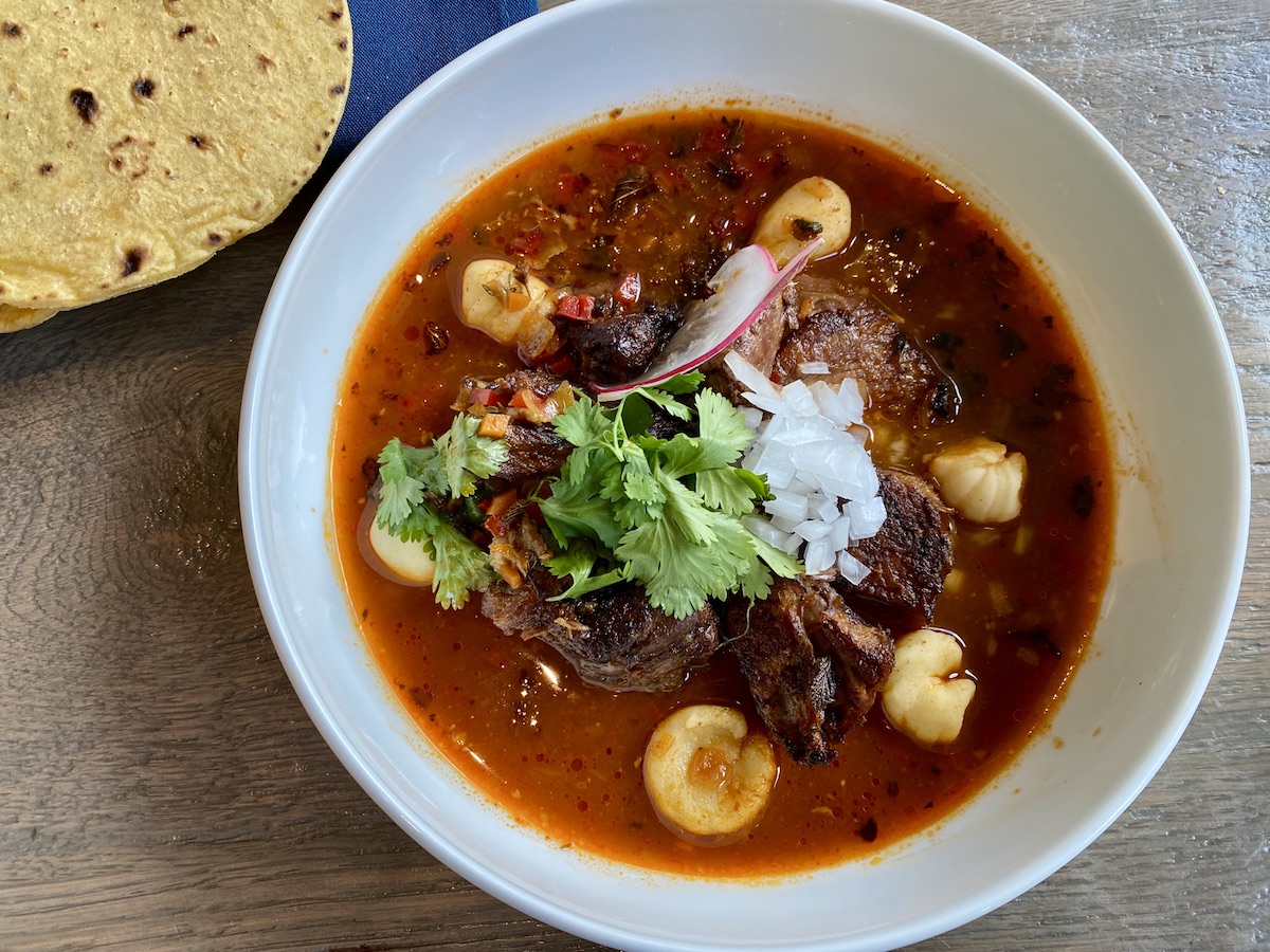 Birria - DiningOut Houston Birria, slow-roasted lamb marinated in chile adobo wrapped in a banana leaf, consommé, onion, and cilantro with corn tortillas at Caracol. | Photo by H-Town Restaurant Group